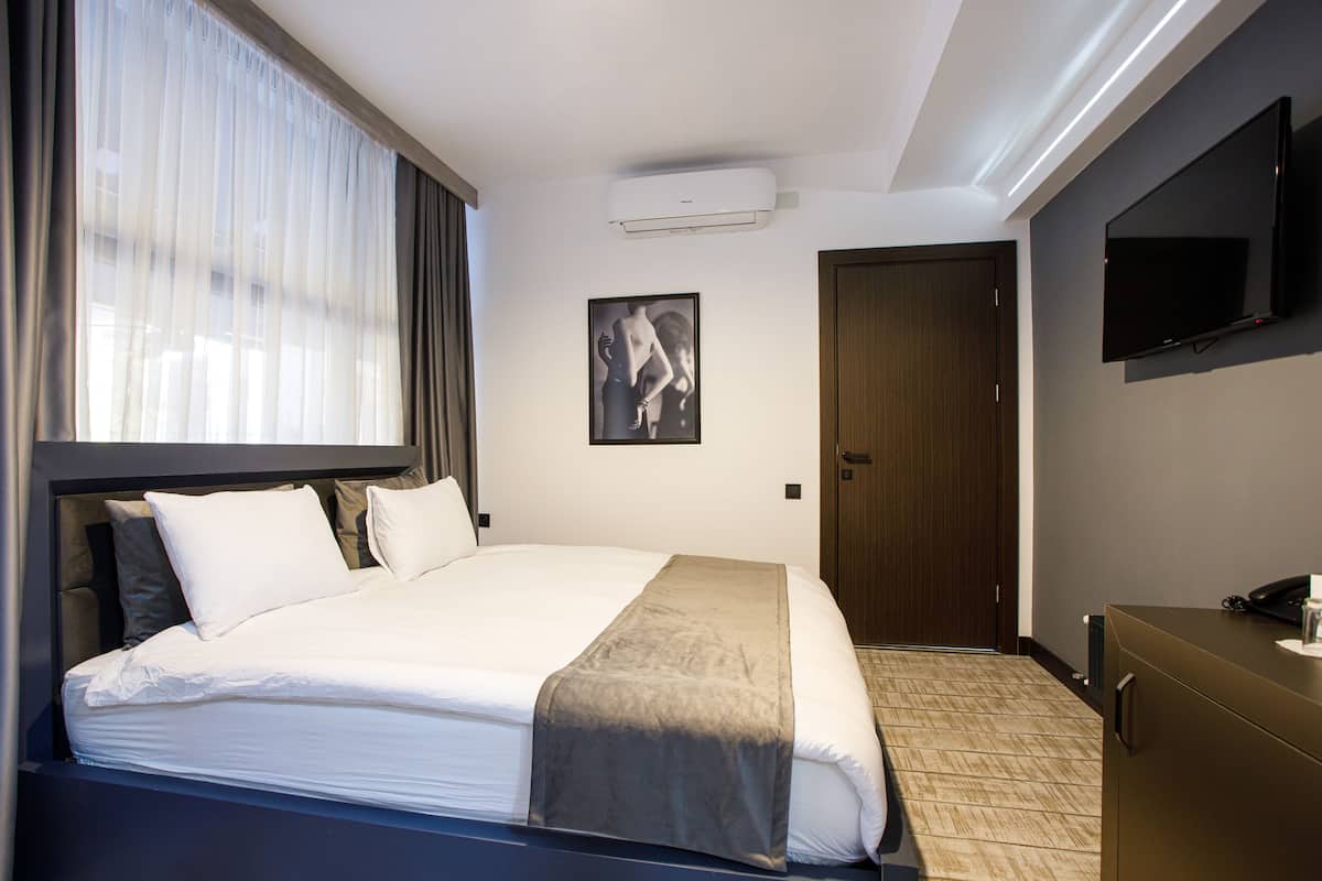 A hotel room with a large bed, a flat-screen TV mounted on the wall, and a wooden door.