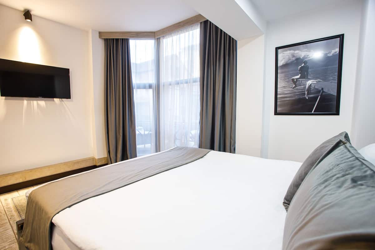 A hotel room with a bed, a flat-screen TV, a large window with curtains, and a framed picture on the wall.