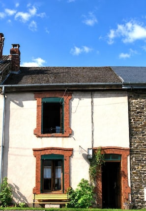 A two-story building with a stone facade, a chimney, and a small porch with a bench. - LE PETIT GÎTE - GESPUNSART (GESPUNSART)