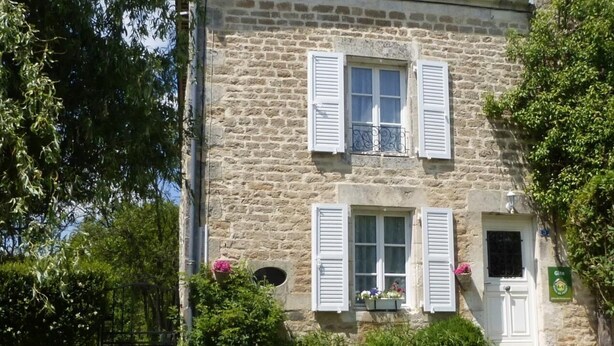 Ein Steinhaus mit weißen Fensterläden, einem Balkon und einer Tür mit einem grünen Schild.