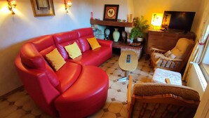 A living room with a red sofa, a wooden chair, a small table, and a TV. - 1843 LE RUISSEAU DU MOULIN (SEUIL)