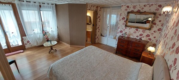 A bedroom with a large bed, a dresser, a vanity with a mirror, and a small table with flowers.
