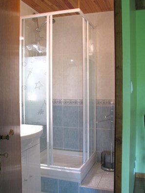 Bathroom features a glass-enclosed shower, white sink, and simple tile pattern.