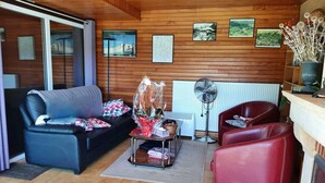 Ein gemütliches Wohnzimmer mit einer schwarzen Couch, einem roten Sessel, einem kleinen Tisch mit Ventilator und einer Heizung.