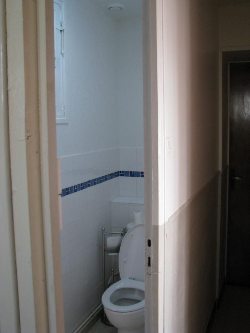 Een smalle gang die leidt naar een badkamer met toilet en douche.