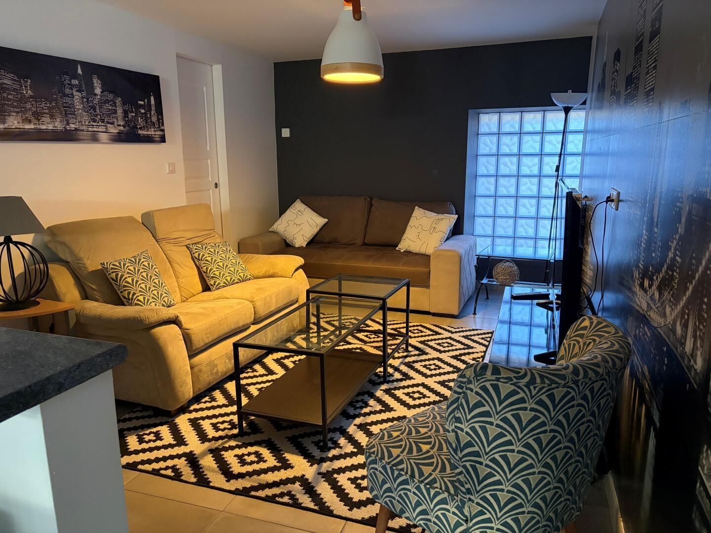 A living room with a sofa, coffee table, patterned rug, and a cityscape painting on the wall.