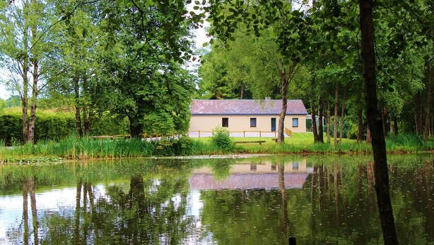 Ett hus vid en stilla damm, med en träveranda och en gräsyta.