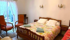A bedroom with a wooden bed, two bedside tables, a chair, a desk, and a chandelier.