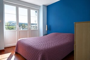 Un dormitorio con una cama, una ventana con vistas y una pared azul.