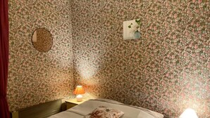 A bedroom with floral wallpaper, a bed with a floral pillow, two bedside tables with lamps, and a mirror on the wall.