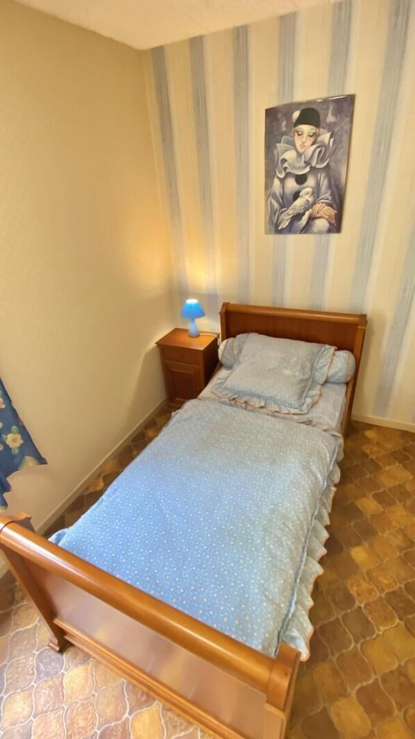 A single bed with a wooden frame, a nightstand with a lamp, and a striped wall with a painting.