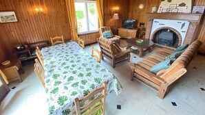 A cozy room with wooden walls, a dining table with chairs, a sofa, a TV, and a fireplace.