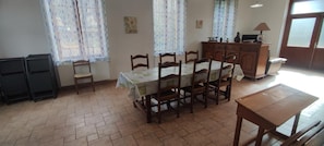 A dining area with a table set for six, wooden chairs, a cabinet with kitchenware, and a window with curtains.