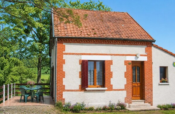 Une petite maison en briques avec un toit en tuiles, une porte d’entrée et une fenêtre avec des volets.