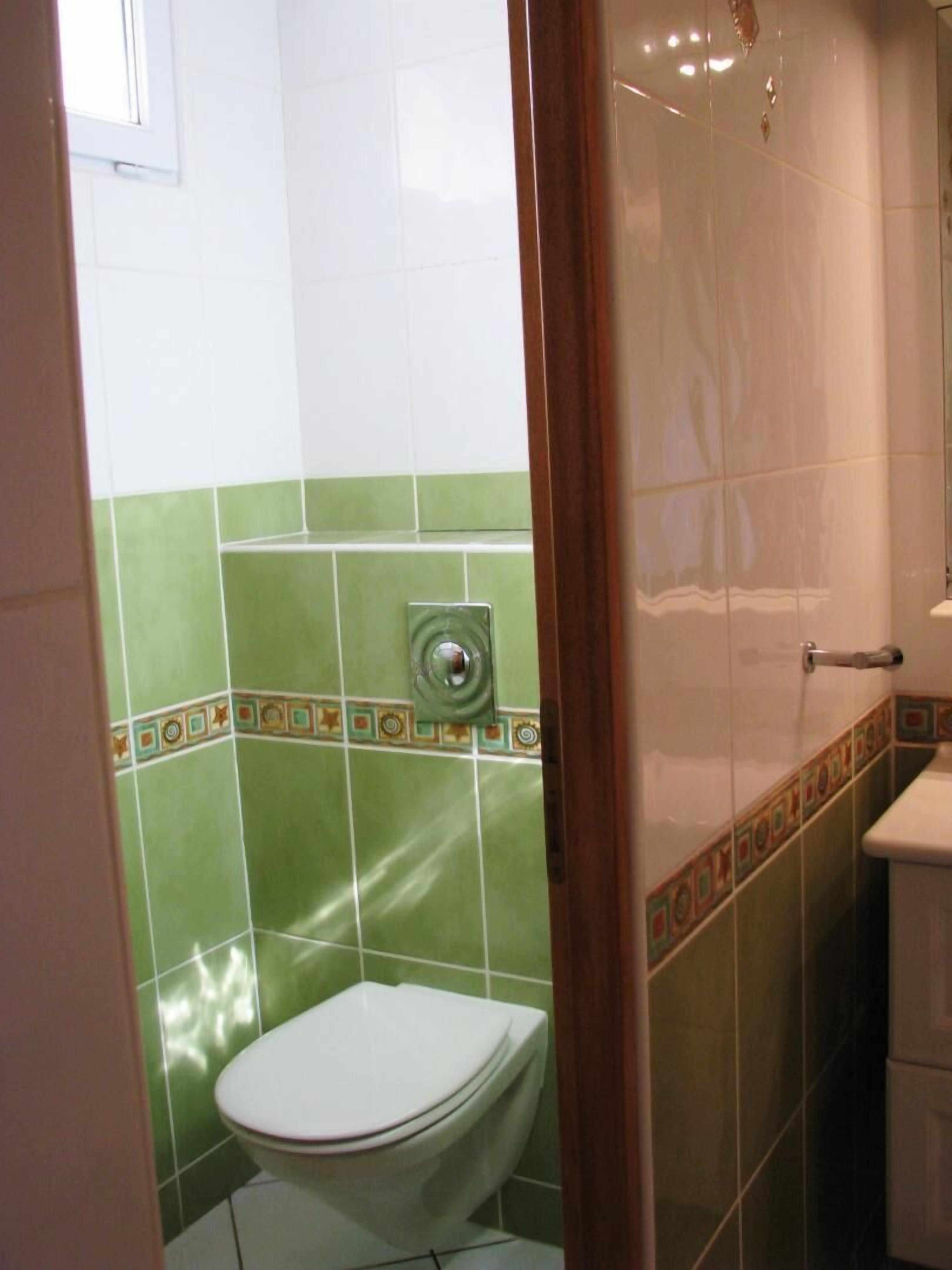 A bathroom with a toilet, green and white tiled walls, and a shower area.