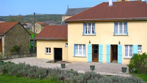Un bâtiment à deux étages, avec un toit recouvert de tuiles rouges, une cheminée en pierre et des volets bleus aux fenêtres.