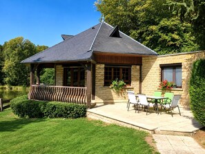 A stone building with a covered patio, a wooden deck, and a view of a lake. - LE COIN DE PARADIS - BAALONS (BAALONS)