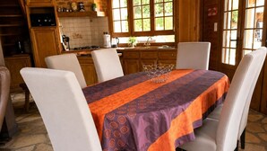 A dining area with a table set for four, surrounded by chairs, in a room with wooden cabinets and a stone floor.
