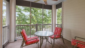 Ein überdachter Balkon mit rundem Tisch und vier Stühlen, großen Fenstern und einem Deckenventilator.
