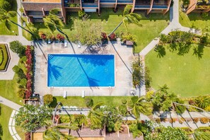 Vista aérea de um resort com uma piscina central, rodeado por jardins bem cuidados e palmeiras.