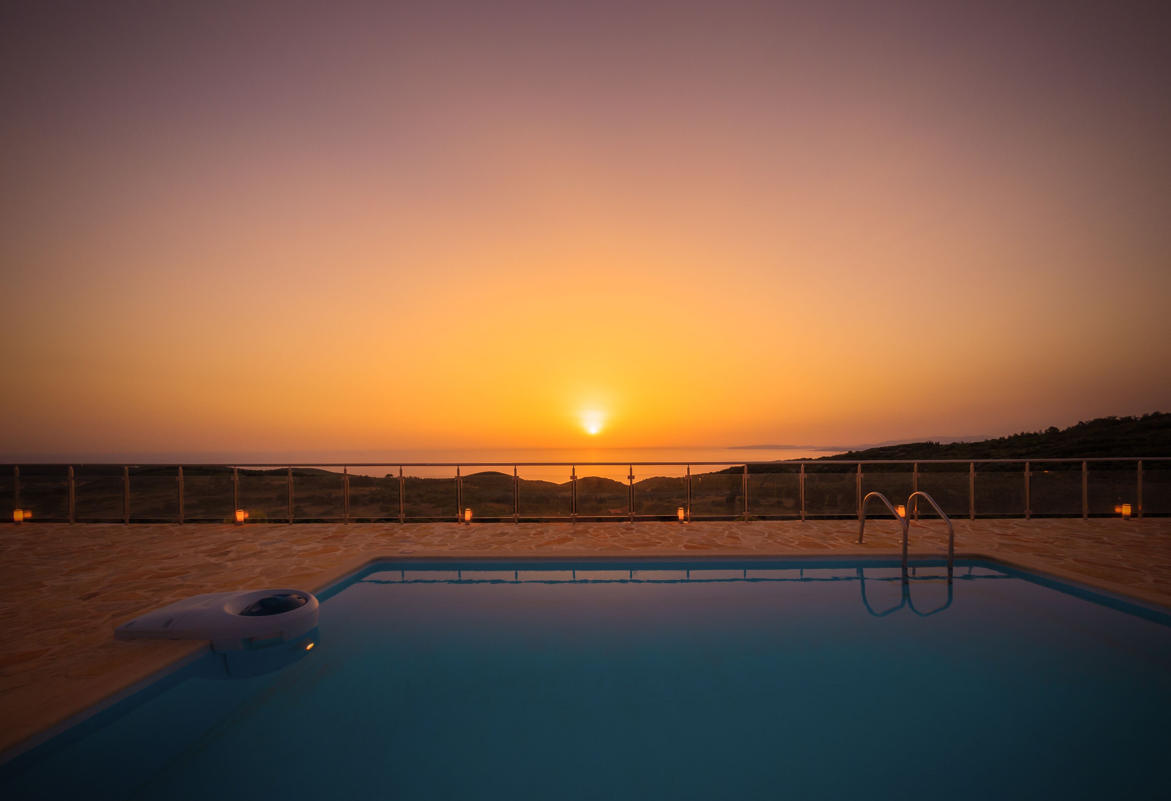 Una piscina con vista al atardecer, rodeada de arena y una valla.