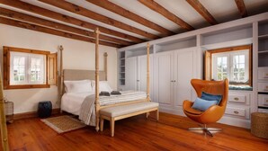 Una camera da letto con un letto a baldacchino, pavimento in legno, un'ampia finestra e mobili contenitori bianchi a muro.