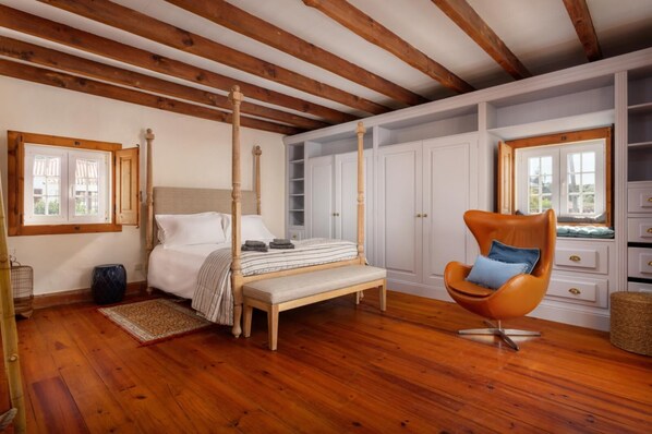 A bedroom with a four-poster bed, wooden flooring, a large window, and built-in white cabinets. - Writer's Cottage Luxury Home Inspiration (Colares)