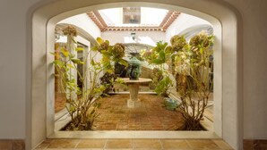 Un arco conduce a un cortile con una fontana, circondato da piante in vaso e un pavimento piastrellato.