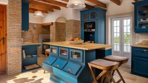 Una cucina con mobili blu, un'isola centrale, sgabelli di legno e una parete in mattoni.