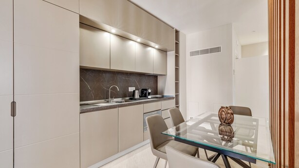 Una cocina moderna con una mesa de comedor de vidrio, armarios color beige y un protector contra salpicaduras de mármol.