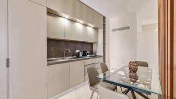 Una cocina moderna con una mesa de comedor de vidrio, armarios color beige y un protector contra salpicaduras de mármol.