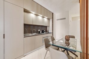 A modern kitchen with a glass dining table, beige cabinetry, and a marble backsplash. - Oriana Homèl Udine (Udine)