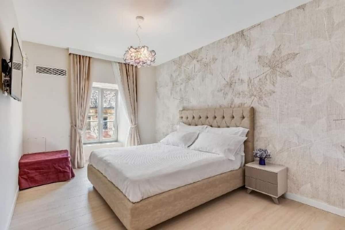 Camera da letto con un letto, un comodino, una finestra con tende e una parete con motivo a foglia.