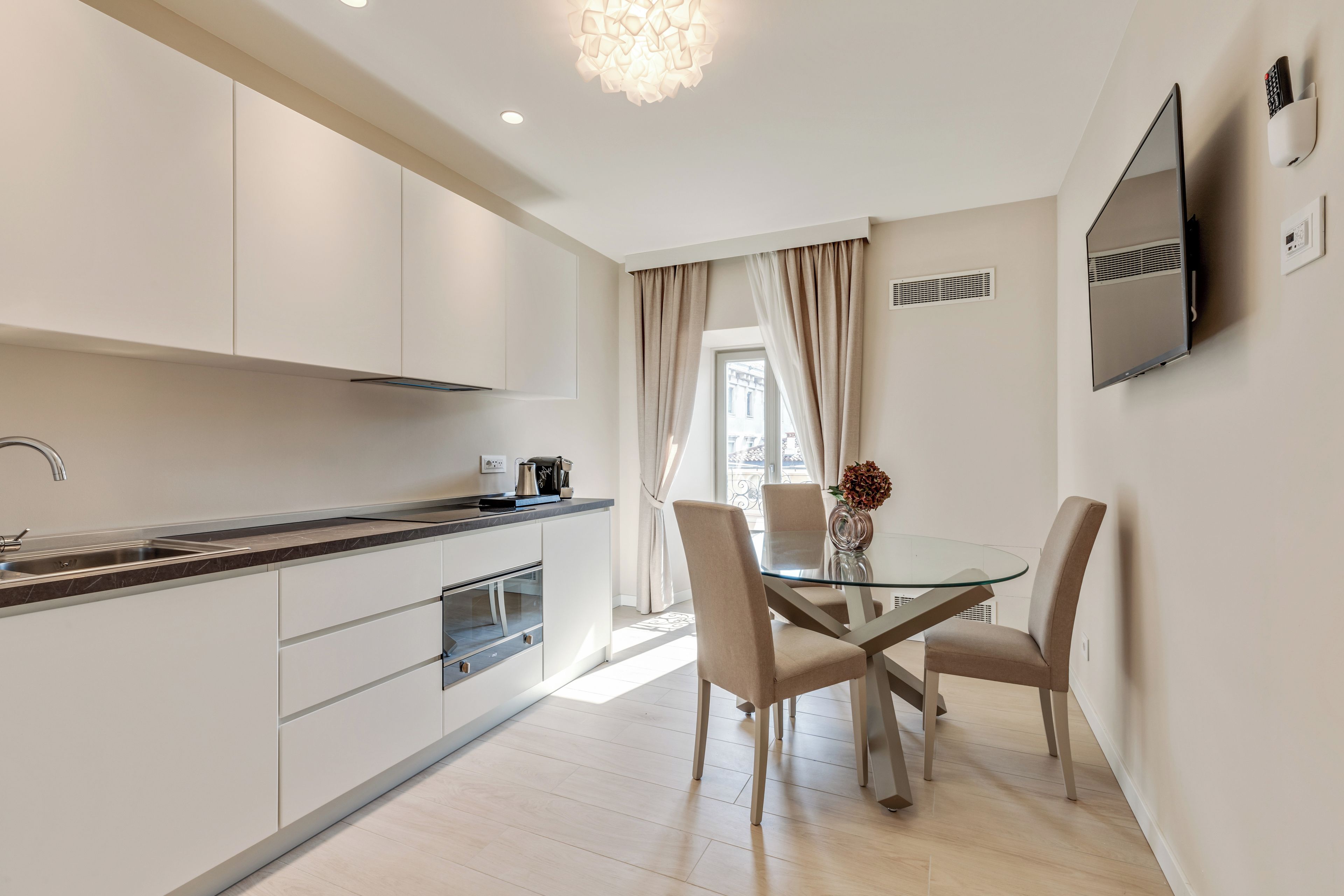 Una cocina moderna con armarios blancos, una mesa de comedor de vidrio y sillas color beige.