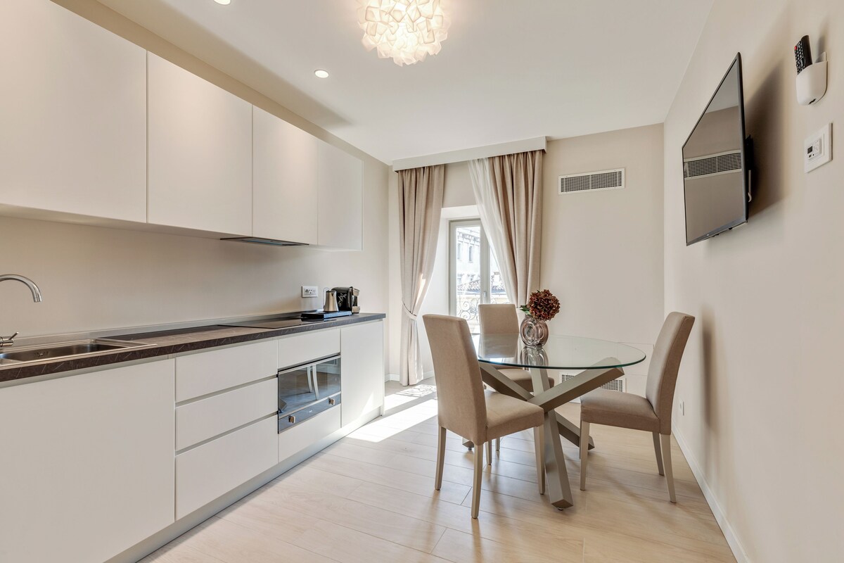 Una cocina moderna con armarios blancos, una mesa de comedor de vidrio y sillas color beige.