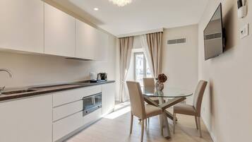 Una cocina moderna con armarios blancos, una mesa de comedor de vidrio y sillas color beige.