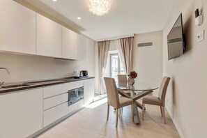 A modern kitchen with white cabinets, a glass-top dining table, and beige chairs. - Oriana Homèl Udine (Udine)