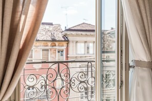 Una ventana con barandillas metálicas y cortinas, que ofrece vistas a edificios de arquitectura tradicional.