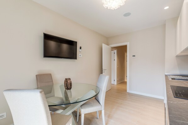 A modern dining area with a glass table, cushioned chairs, a mounted flat-screen TV, and a hallway leading to another room. - Oriana Homèl Udine (Udine)