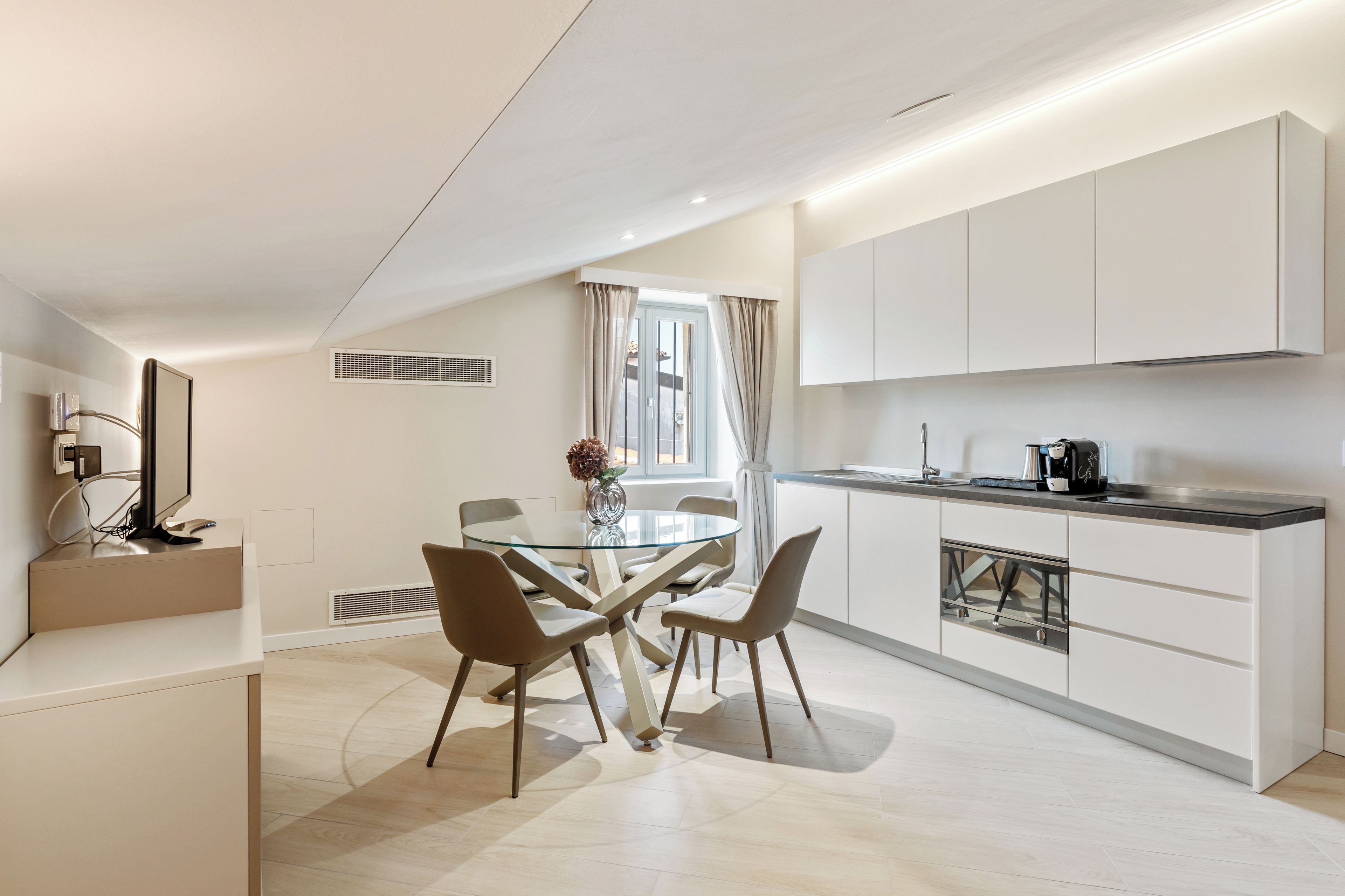 Una cocina moderna con comedor, que incluye una mesa de vidrio, sillas y una cafetera.