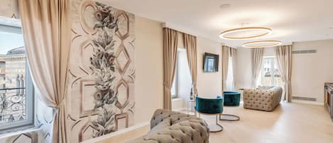 A modern living room with a large sectional sofa, a tufted ottoman, and a teal armchair. The room features a large window with curtains, a decorative wall mural, and a circular ceiling light fixture.