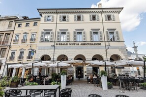 Un edificio con un letrero que dice "S. Reale Mutua Assicurazioni" y terraza exterior con sombrillas.
