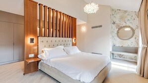 Un dormitorio moderno con una cama grande, cabecera de madera, mesitas de noche, un banco empotrado, un espejo redondo y una lámpara decorativa.