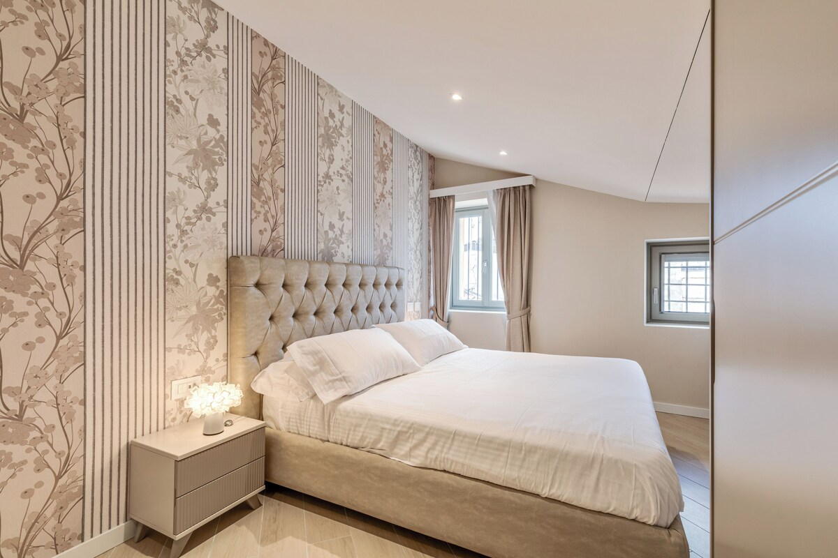 A bedroom with a large bed, a nightstand with a lamp, and a window with curtains.