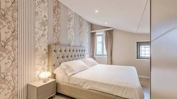 A bedroom with a large bed, a nightstand with a lamp, and a window with curtains.