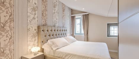Un dormitorio con una cama grande, una mesita de noche con lámpara y una ventana con cortinas.