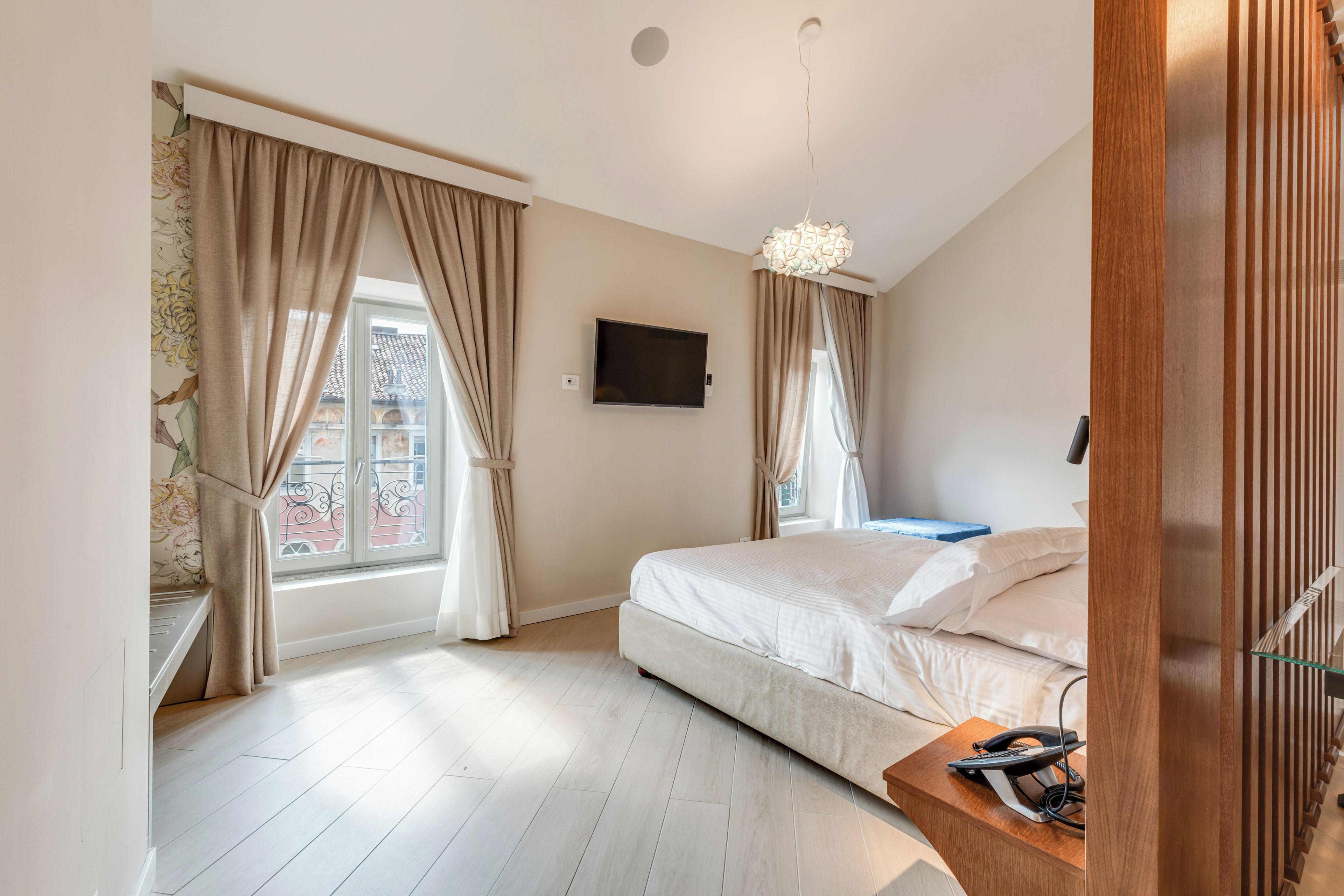 Un dormitorio con cama, televisión montada en la pared y ventana con cortinas.