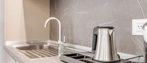 Una cucina con un bollitore moderno in acciaio inossidabile su un vassoio, un rubinetto e una presa di corrente sul piano di lavoro.