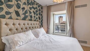 Una habitación de hotel con cabecera capitonada, un ventanal con vistas a edificios y un papel tapiz estampado.