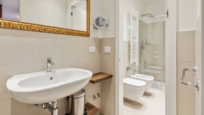 Un baño moderno con un lavamanos grande de color blanco, un espejo con marco dorado y una zona de ducha con mampara de vidrio.